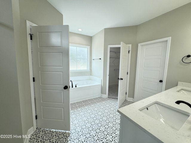 full bath featuring a sink, baseboards, a bath, and a spacious closet