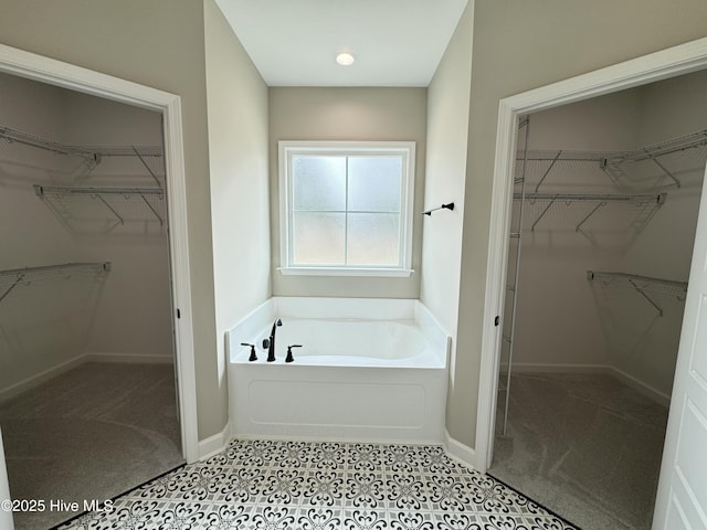 bathroom with a garden tub, a spacious closet, and baseboards