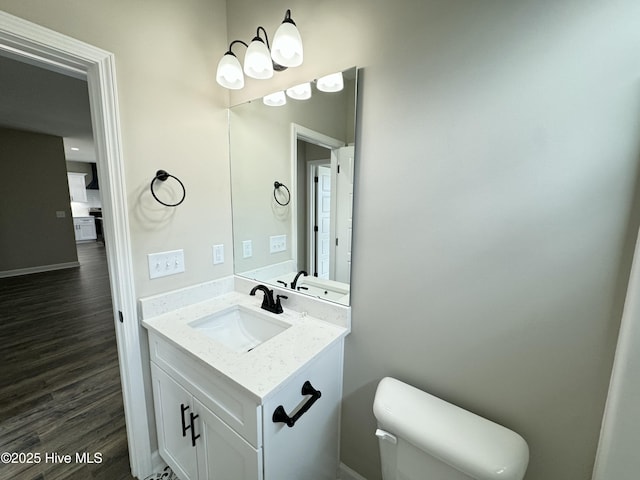 half bath featuring baseboards, toilet, wood finished floors, and vanity