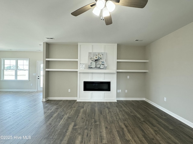 unfurnished living room with a glass covered fireplace, dark wood finished floors, visible vents, and baseboards