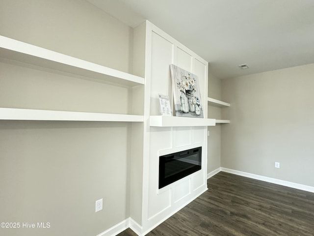 unfurnished living room featuring a glass covered fireplace, baseboards, visible vents, and dark wood-style flooring