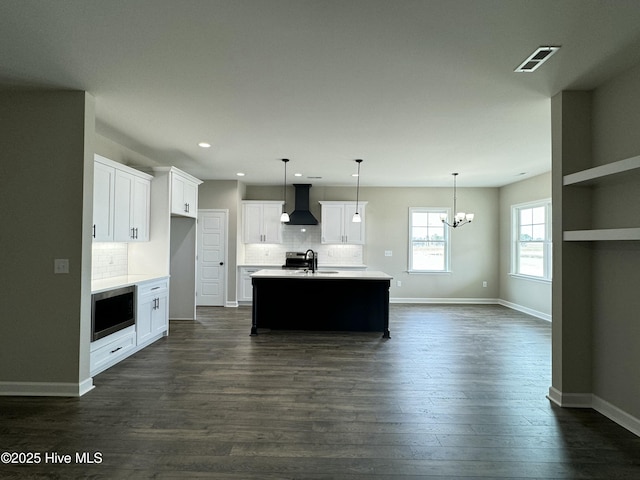 kitchen with stainless steel microwave, wall chimney range hood, light countertops, dark wood-style floors, and a sink