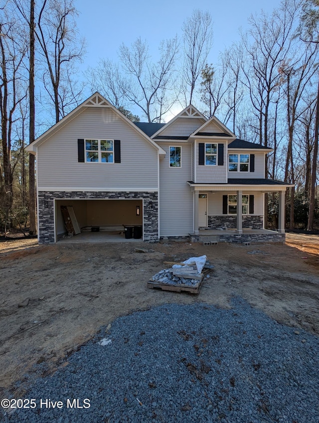 view of front of property with stone siding, an attached garage, covered porch, and driveway