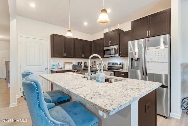 kitchen with a kitchen breakfast bar, sink, an island with sink, appliances with stainless steel finishes, and decorative light fixtures