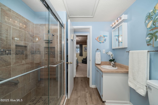 full bath featuring a textured ceiling, toilet, wood finished floors, vanity, and a shower stall