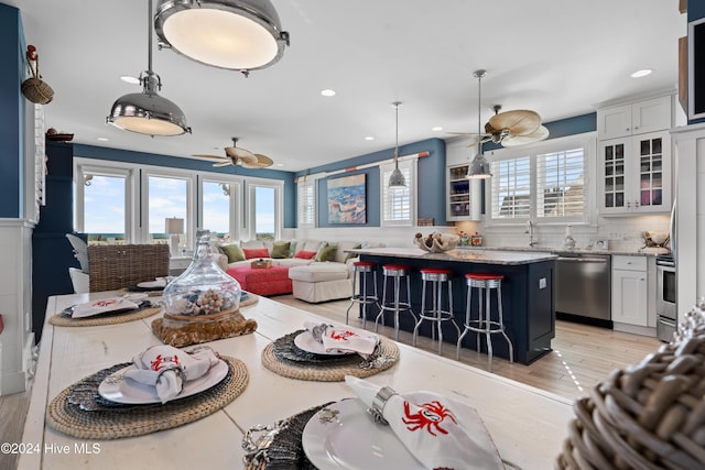 kitchen featuring light wood-type flooring, stainless steel dishwasher, decorative light fixtures, white cabinets, and a kitchen island