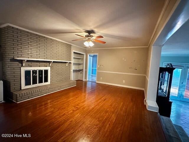 unfurnished living room with hardwood / wood-style flooring, built in shelves, ornamental molding, and a brick fireplace