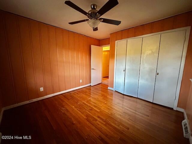 unfurnished bedroom with ceiling fan, wood-type flooring, wooden walls, and a closet