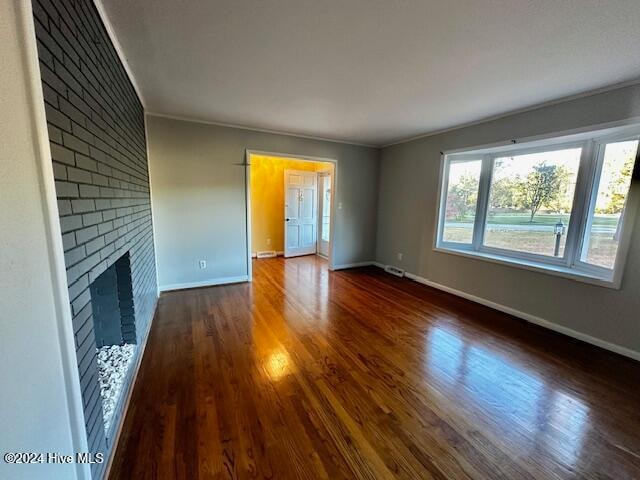 unfurnished living room with dark hardwood / wood-style floors, a brick fireplace, and crown molding