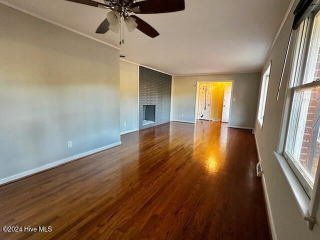 interior space with ceiling fan, ornamental molding, dark wood-type flooring, and a brick fireplace