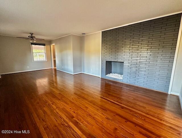 unfurnished living room with ceiling fan, a brick fireplace, brick wall, hardwood / wood-style floors, and ornamental molding