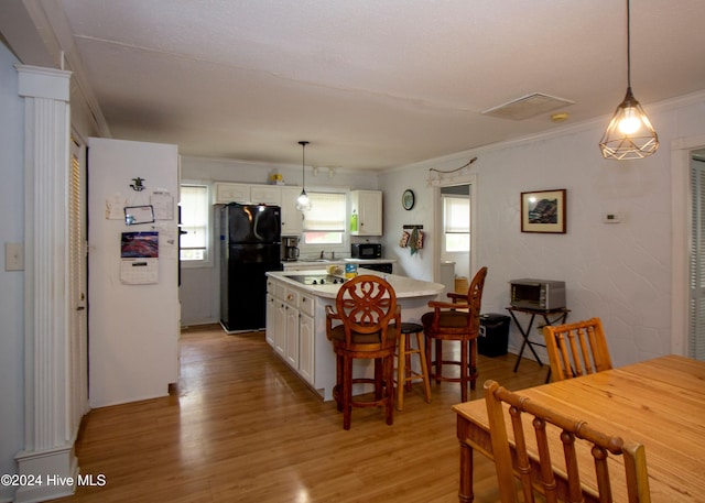 kitchen with black refrigerator, light wood-type flooring, white cabinetry, and a wealth of natural light