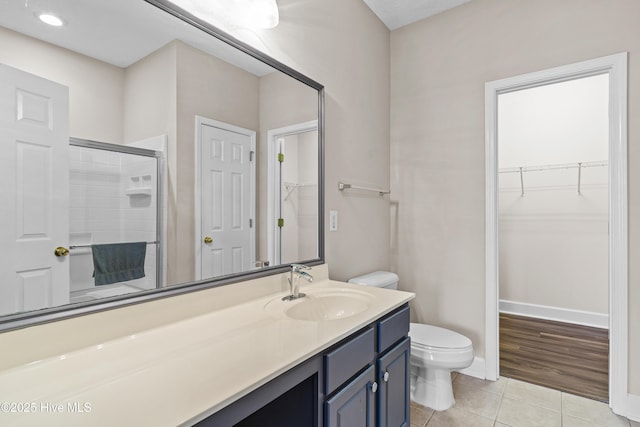 bathroom featuring tile patterned flooring, vanity, a shower with shower door, and toilet