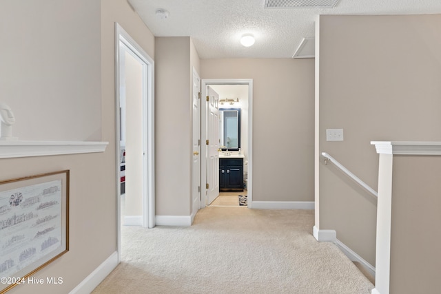 hall with light colored carpet and a textured ceiling