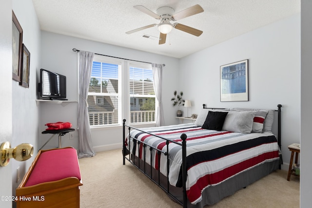 bedroom with ceiling fan, light colored carpet, and a textured ceiling