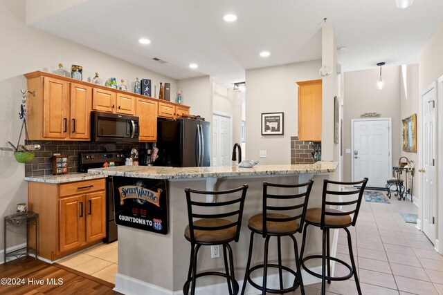 kitchen with black refrigerator, stainless steel range with electric stovetop, a kitchen breakfast bar, light stone counters, and kitchen peninsula