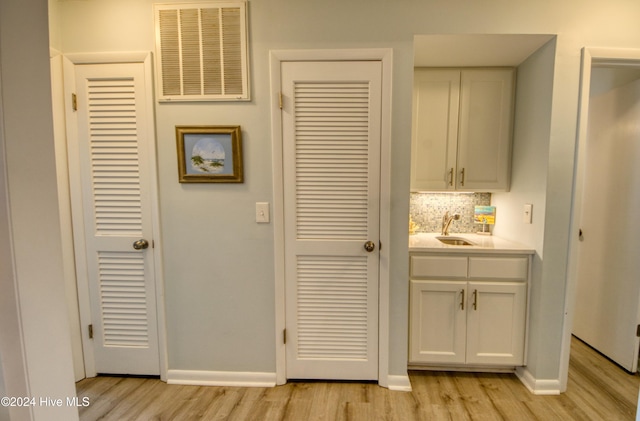 kitchen featuring light wood-type flooring, tasteful backsplash, white cabinetry, and sink