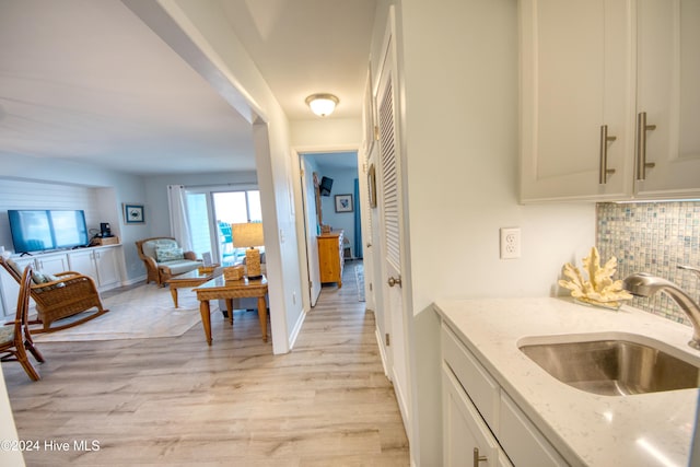 kitchen featuring backsplash, light stone counters, sink, light hardwood / wood-style flooring, and white cabinets