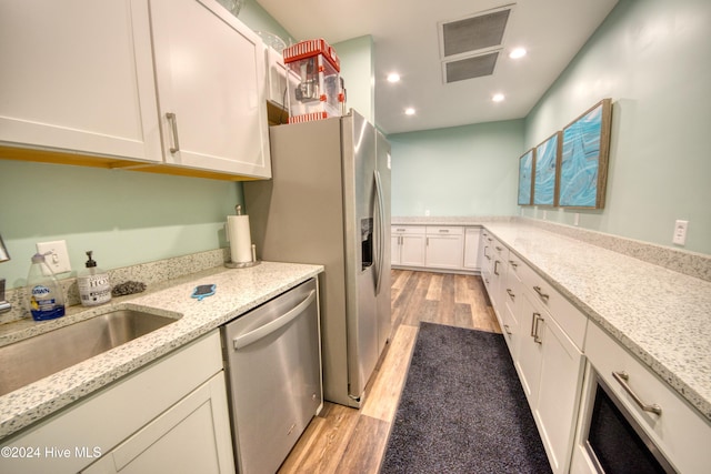 kitchen with white cabinets, light stone counters, appliances with stainless steel finishes, and light hardwood / wood-style flooring