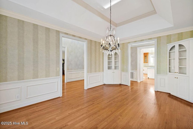 unfurnished dining area with a tray ceiling, crown molding, light wood-type flooring, and an inviting chandelier