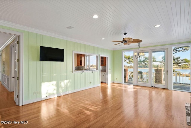 unfurnished living room featuring ceiling fan with notable chandelier, a water view, ornamental molding, and light wood-type flooring