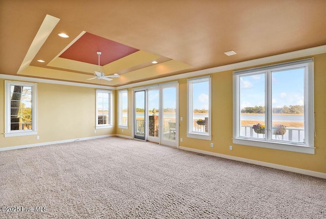 interior space featuring a tray ceiling, carpet floors, ceiling fan, and a water view