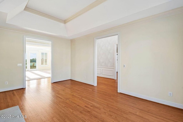 empty room featuring a tray ceiling, light hardwood / wood-style flooring, and ornamental molding