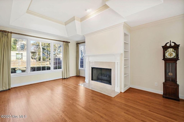 unfurnished living room featuring built in shelves, a raised ceiling, a high end fireplace, wood-type flooring, and ornamental molding