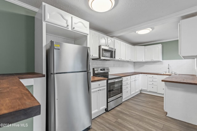 kitchen with white cabinets, appliances with stainless steel finishes, light wood-type flooring, and ornamental molding