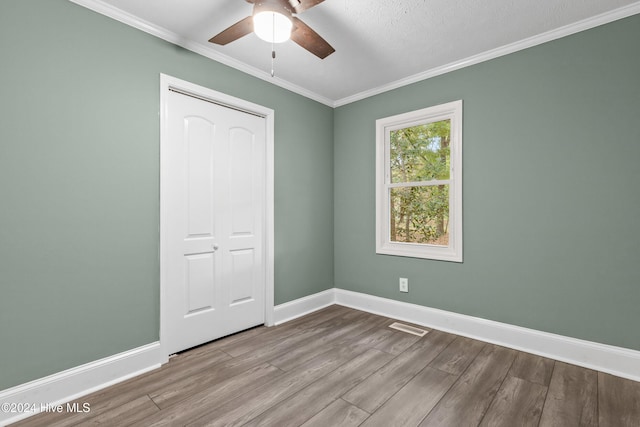 unfurnished bedroom with ceiling fan, a closet, ornamental molding, and light wood-type flooring