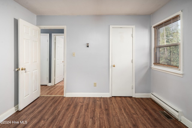 unfurnished bedroom with dark hardwood / wood-style floors and a baseboard heating unit