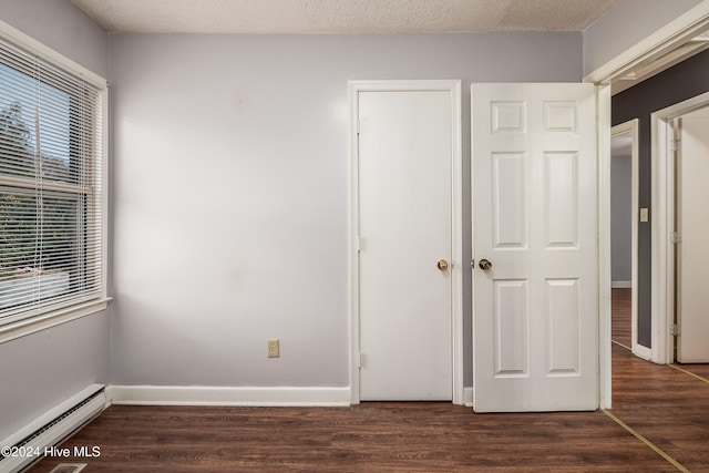 unfurnished bedroom with baseboard heating, dark hardwood / wood-style flooring, and a textured ceiling