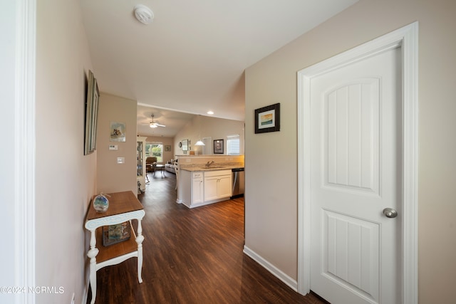 hall featuring a sink, baseboards, lofted ceiling, and dark wood-type flooring