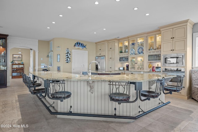 kitchen with cream cabinetry, a breakfast bar, light stone counters, and appliances with stainless steel finishes