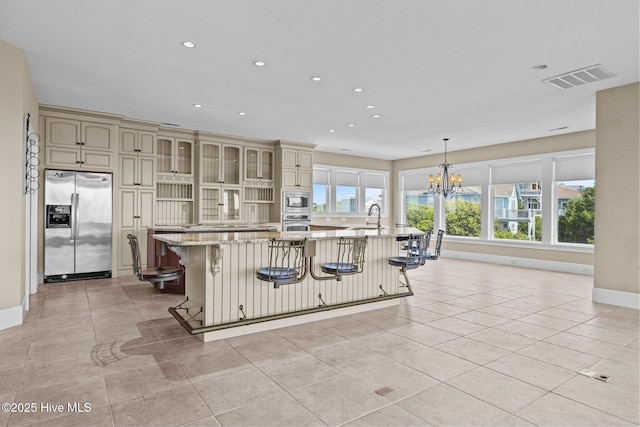 10108 Sea Breeze Dr, Emerald Isle, NC 28594 - kitchen featuring cream cabinets, stainless steel appliances, a chandelier, light tile patterned flooring, and a kitchen breakfast bar