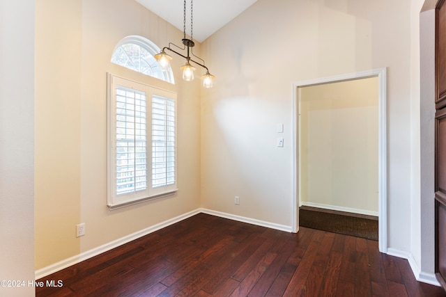 spare room with dark wood-type flooring, vaulted ceiling, and an inviting chandelier