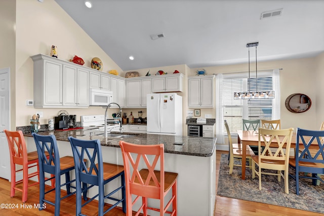 kitchen with white appliances, hanging light fixtures, light hardwood / wood-style flooring, a kitchen bar, and white cabinetry