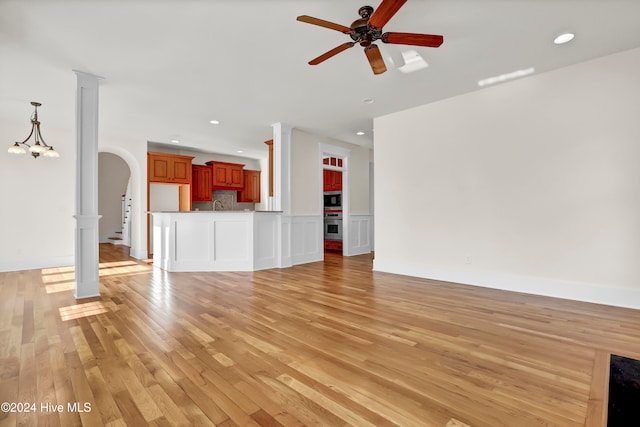 unfurnished living room with ceiling fan with notable chandelier and light hardwood / wood-style floors