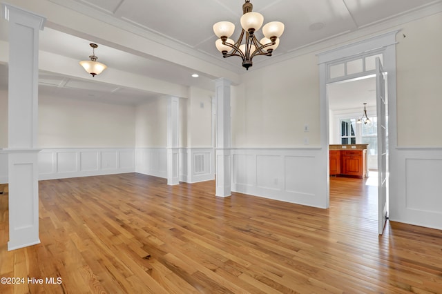 unfurnished dining area with decorative columns, ornamental molding, light hardwood / wood-style flooring, and a chandelier