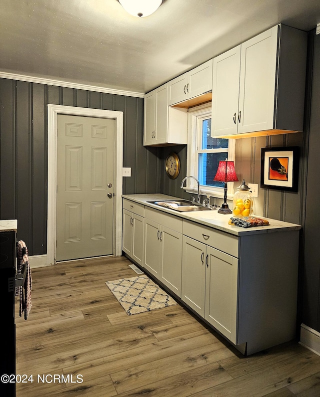 kitchen with white cabinets, crown molding, sink, and light hardwood / wood-style flooring