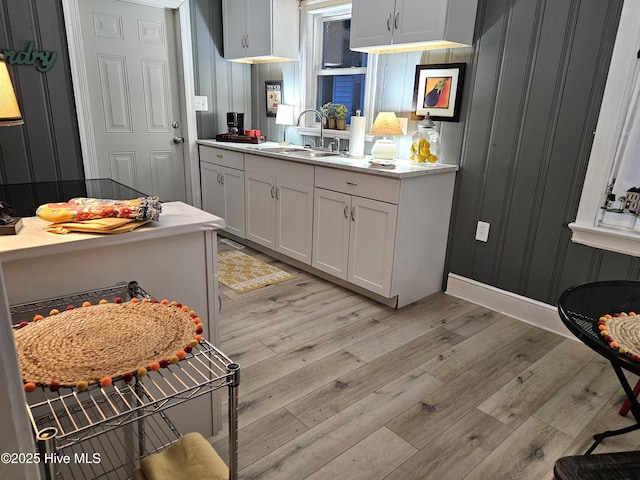 kitchen featuring light wood-type flooring, white cabinets, light countertops, and a sink