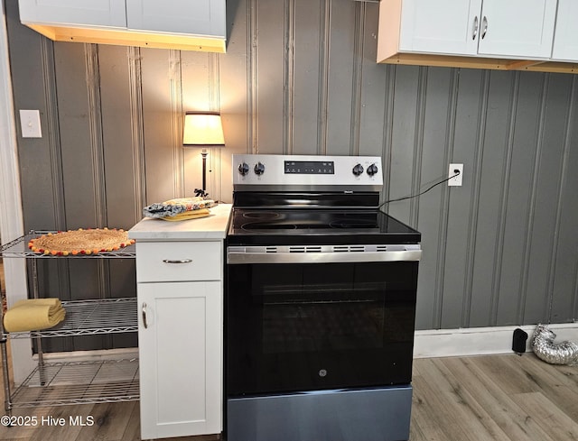 kitchen with electric range, white cabinets, light countertops, and wood finished floors