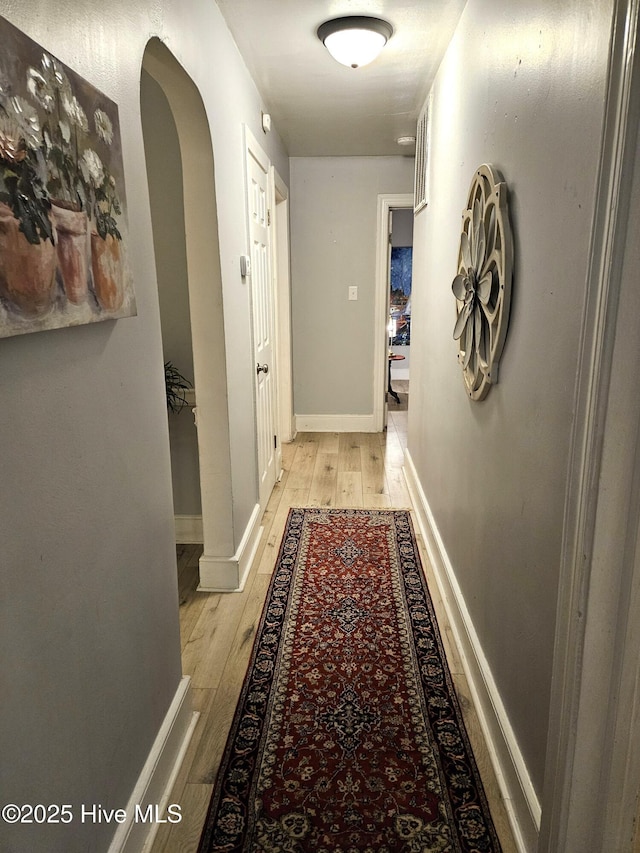 corridor featuring light wood-style flooring, arched walkways, and baseboards