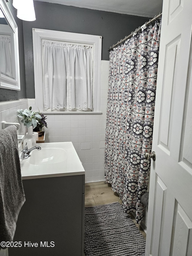 full bathroom with a shower with shower curtain, wainscoting, wood finished floors, vanity, and tile walls