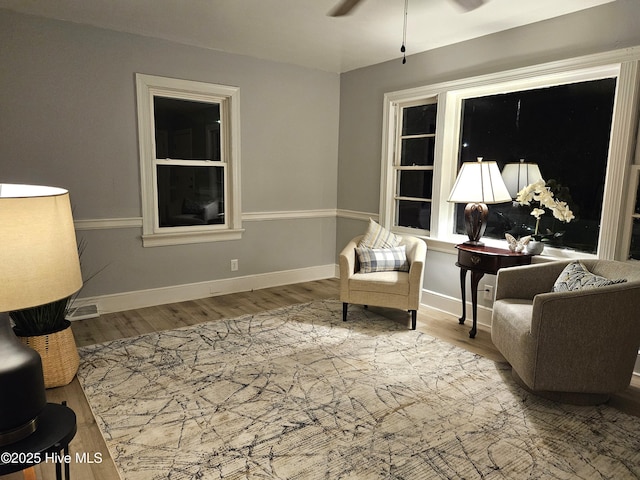 living area with a ceiling fan, baseboards, and wood finished floors