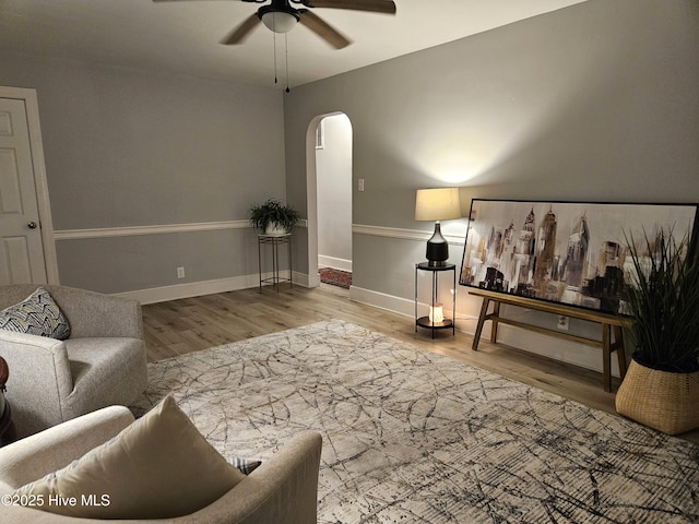 living area with a ceiling fan, baseboards, arched walkways, and wood finished floors