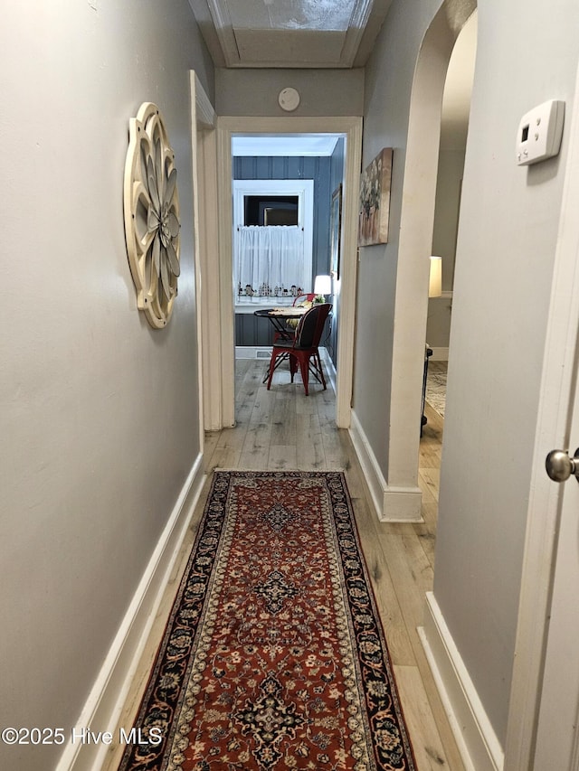 hall with arched walkways, light wood finished floors, and baseboards