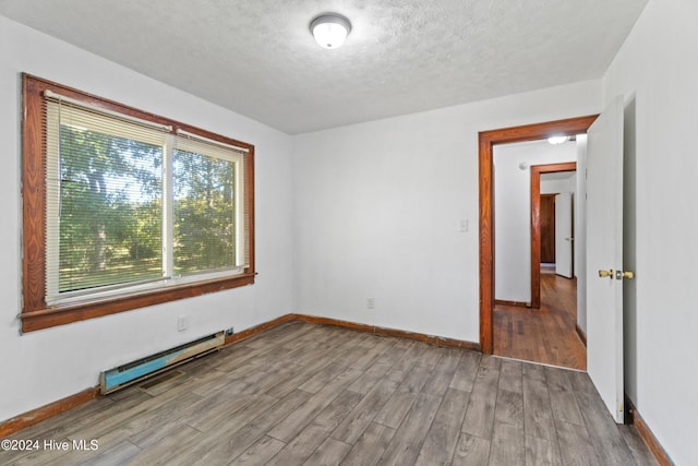 spare room featuring a baseboard heating unit, a textured ceiling, and light wood-type flooring