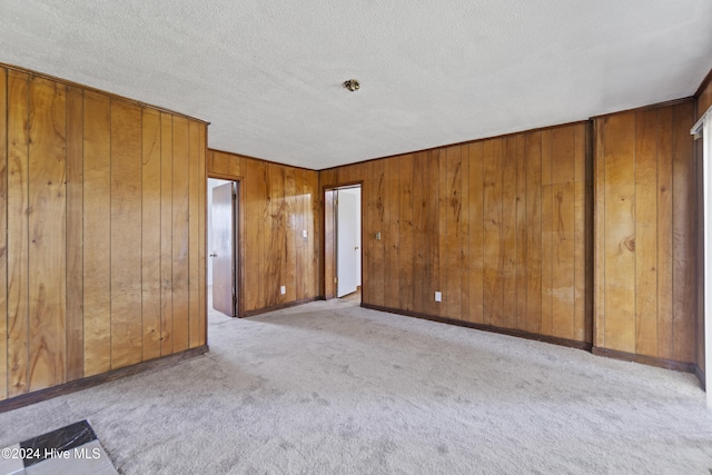 spare room featuring wooden walls, light carpet, and a textured ceiling