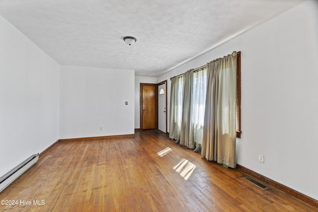 empty room featuring a baseboard radiator, hardwood / wood-style floors, and a textured ceiling